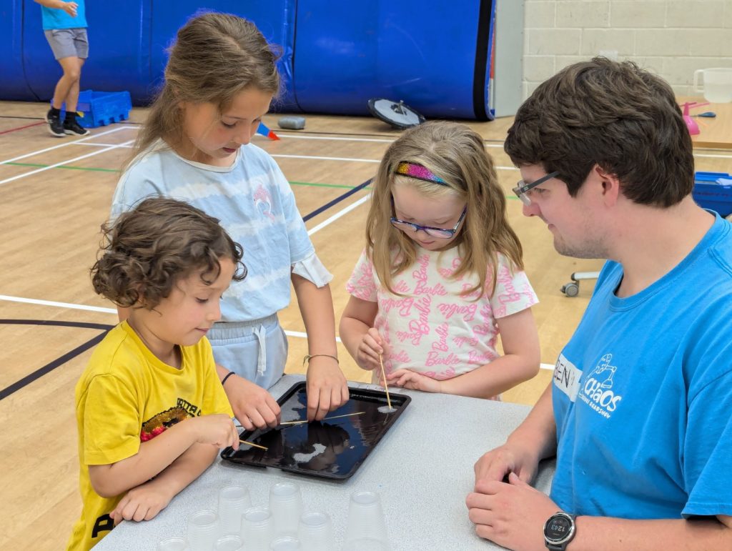 Three children and one CHaOS demonstrator modelling crystal structures using a tray of soap bubbles.